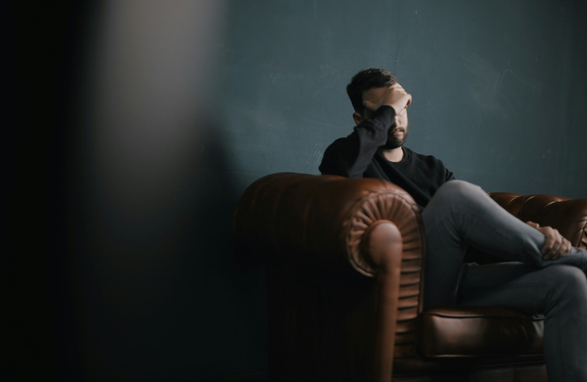 Man sitting on a couch resting his head in his hand, representing fatigue from low testosterone